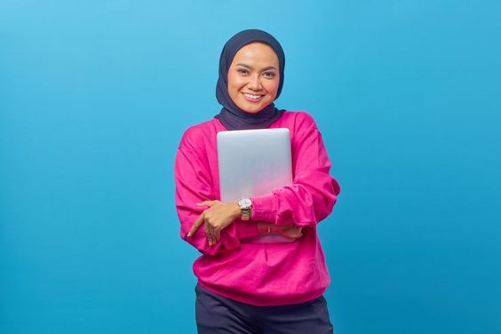 Portrait of beautiful smiling college student wearing pink sweater holding laptop